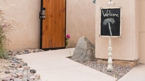 Eine Holztür, ein Willkommensschild und ein kleiner Garten mit Steinen und Pflanzen.