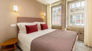 A neatly made bed with a patterned bedspread and two pillows, a small wooden nightstand, and two wall-mounted lamps.