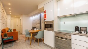 A modern kitchen with white cabinets, a built-in microwave, and a stainless steel oven. There is a dining area with a wooden table and chairs.