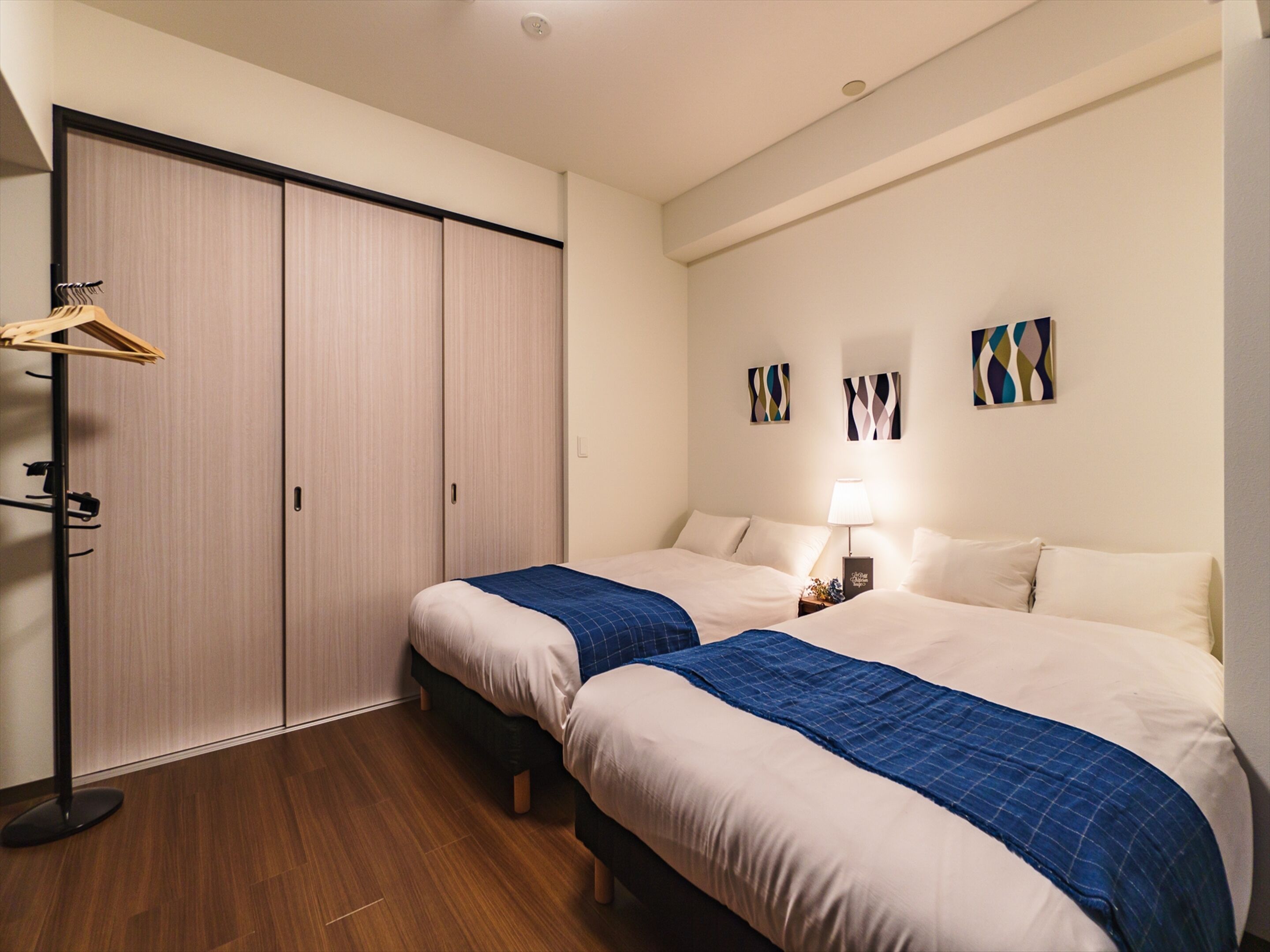 A hotel room with two beds, a wardrobe, and artwork on the wall.