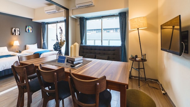 Habitación de hotel con zona de comedor, dos camas, un espejo grande y una ventana con cortinas.