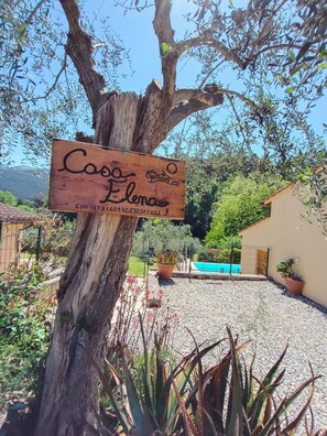 A wooden sign with 'Casa Elena' and a PIN code, a tree, a pool, and a fenced area with potted plants. - CASA ELENA - Detached house with enclosed garden, swimming pool at exclusive use (Lucca)