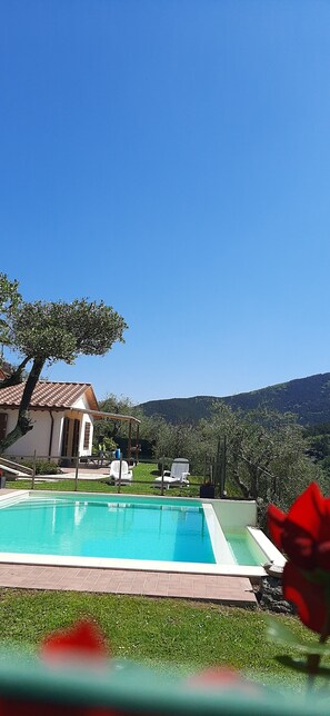 A swimming pool with a clear blue sky, a house with a tiled roof, and a mountainous landscape in the background. - CASA ELENA - Detached house with enclosed garden, swimming pool at exclusive use (Lucca)