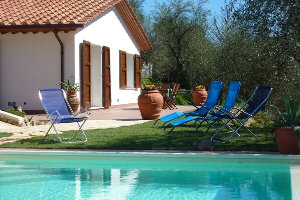 A pool area with blue lounge chairs and a white building with a tiled roof. - CASA ELENA - Detached house with enclosed garden, swimming pool at exclusive use (Lucca)