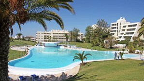 A large swimming pool with a curved edge, surrounded by lounge chairs and palm trees.