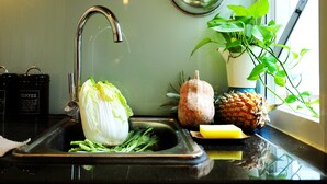 A kitchen sink with a faucet, a colander, a cabbage, a pineapple, and a plant in a white pot. - Chez Tram Homestay (Hanoi)
