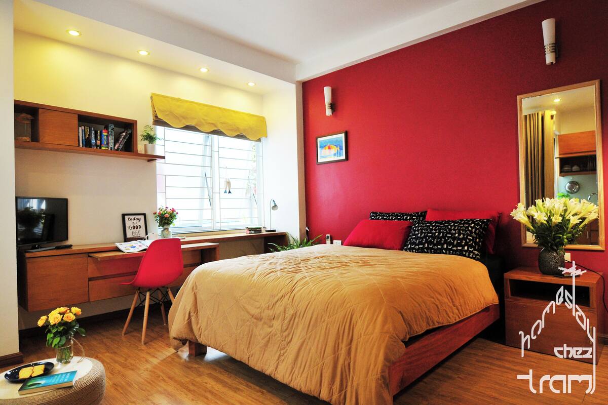 A bedroom with a bed, a desk, a chair, a TV, and a window with curtains.