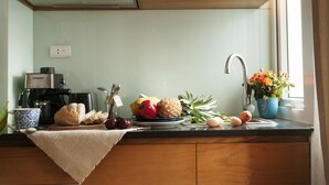 A kitchen with a coffee maker, a sink, and various fruits and vegetables on the counter. - Chez Tram Homestay (Hanoi)