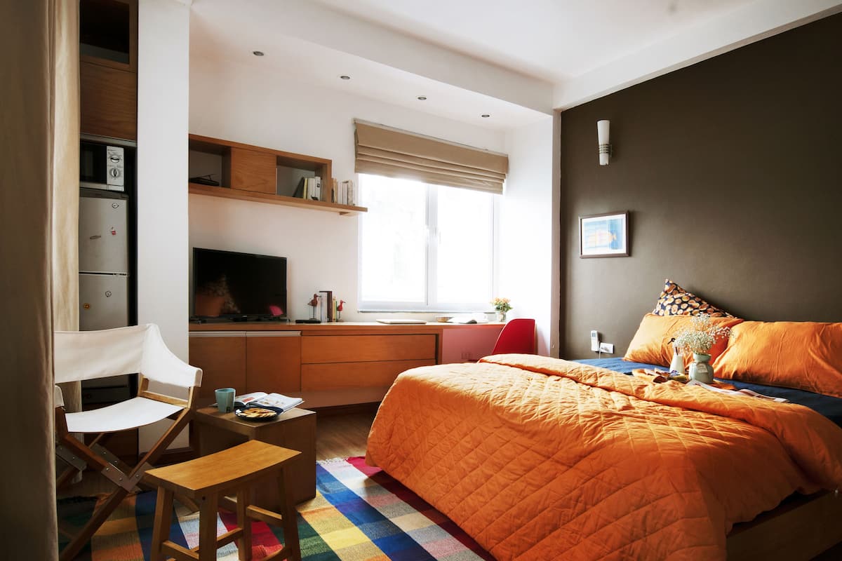 A bedroom with a bed, a desk, a chair, and a window with blinds.