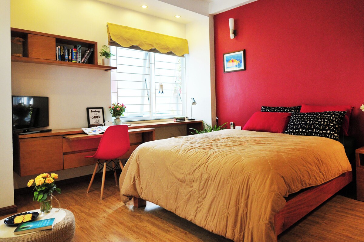 A bedroom with a bed, a desk, a chair, a TV, and a window with curtains.