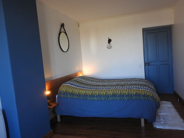 A bedroom with a bed, a nightstand, a wall-mounted lamp, a door, and a small rug. - Farm in a Cluniac village (Pommiers)