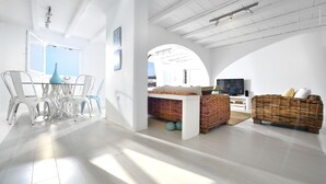 A bright, open living area with a dining table and chairs, a television, and wicker furniture. - Villa Blanca Duo (Mykonos)