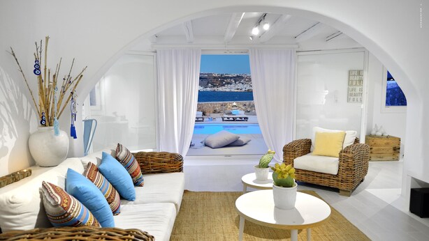 A modern living room with a view of the sea, white furniture, and a wicker chair. - Villa Blanca Duo (Mykonos)