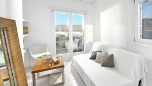 A bright, white room with a wooden table, a white sofa, and a view through a glass door. - Villa Blanca Duo (Mykonos)
