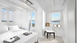 A white room with a bed, a chair, and a window with a view. - Villa Blanca Duo (Mykonos)
