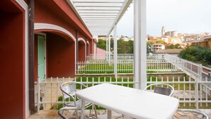 A balcony with a white table and chairs, a white fence, and a view of a cityscape with buildings and a church. - S052 - Sirolo, new studio apartment with terrace (Sirolo)