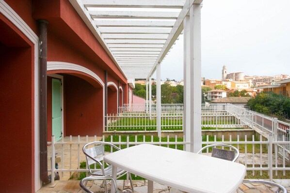 A balcony with a white table and chairs, a white fence, and a view of a cityscape with buildings and a church.