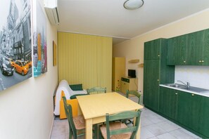 Una cocina compacta con armarios verdes, una mesa amarilla y un comedor.