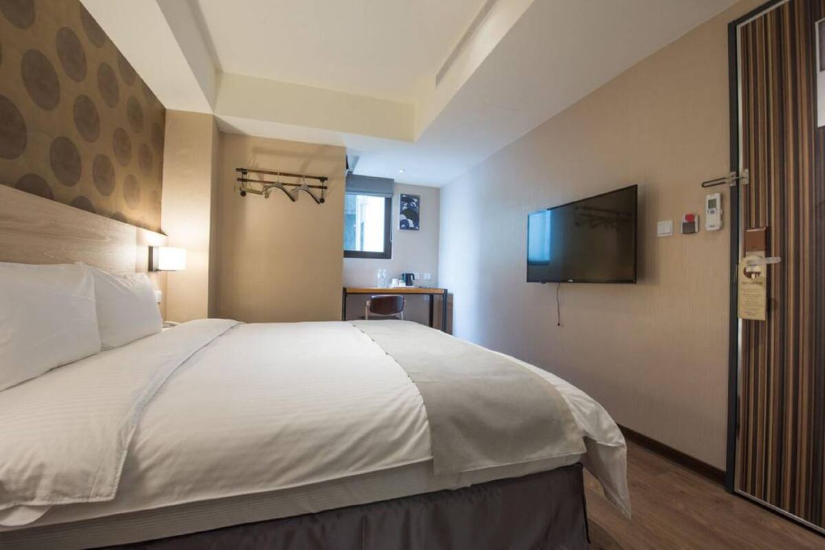A hotel room with a large bed, a desk with a chair, a television mounted on the wall, and a door with a striped pattern.