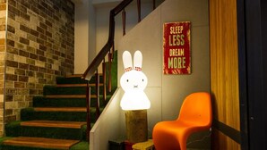 A staircase with a wooden finish and green carpeted steps, a bright white wall-mounted lamp, an orange chair, and a 'SLEEP LESS DREAM MORE' sign. - Lucky Apple Hotel (Taipei)
