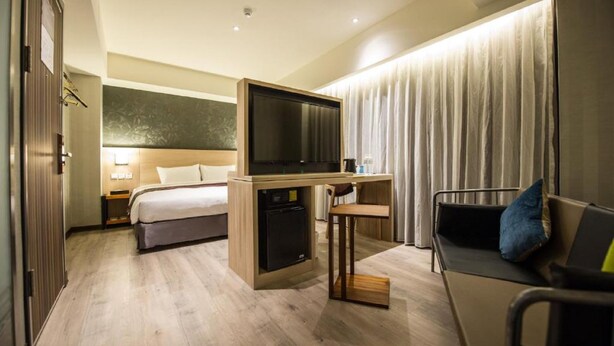 A hotel room with a bed, a desk with a TV, a chair, and a sofa. - Lucky Apple Hotel (Taipei)