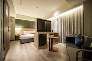 Una habitación de hotel con cama, escritorio con televisor, una silla y un sofá.