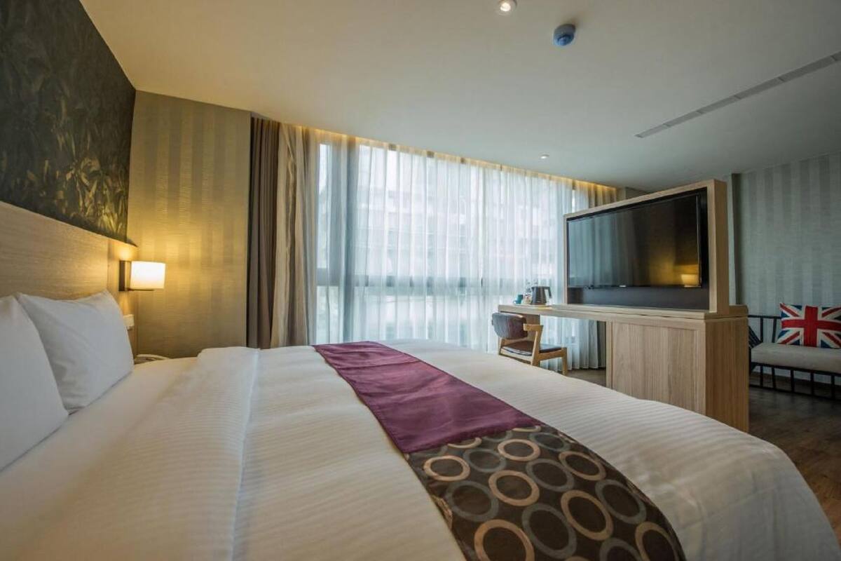 A hotel room with a large bed, a desk with a chair, a television, and a window with curtains.