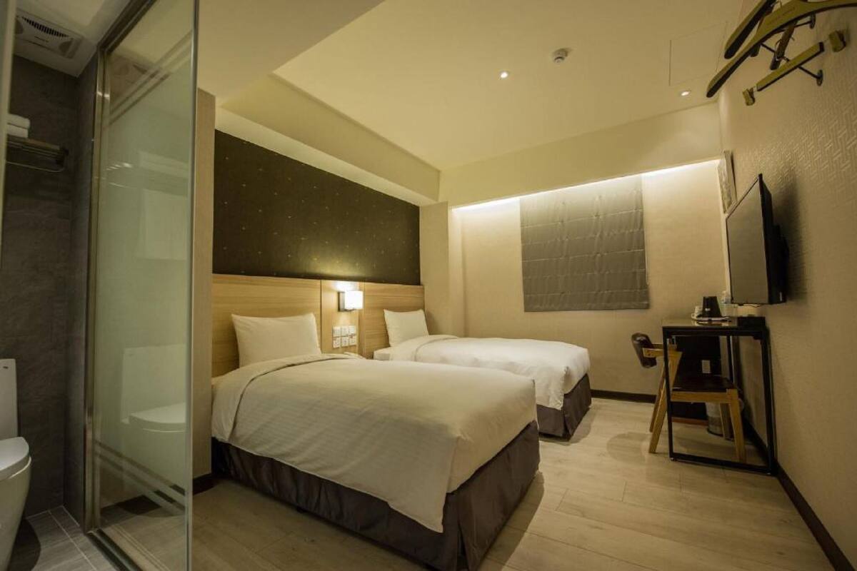 A hotel room with two beds, a shower, a television, and a small table.