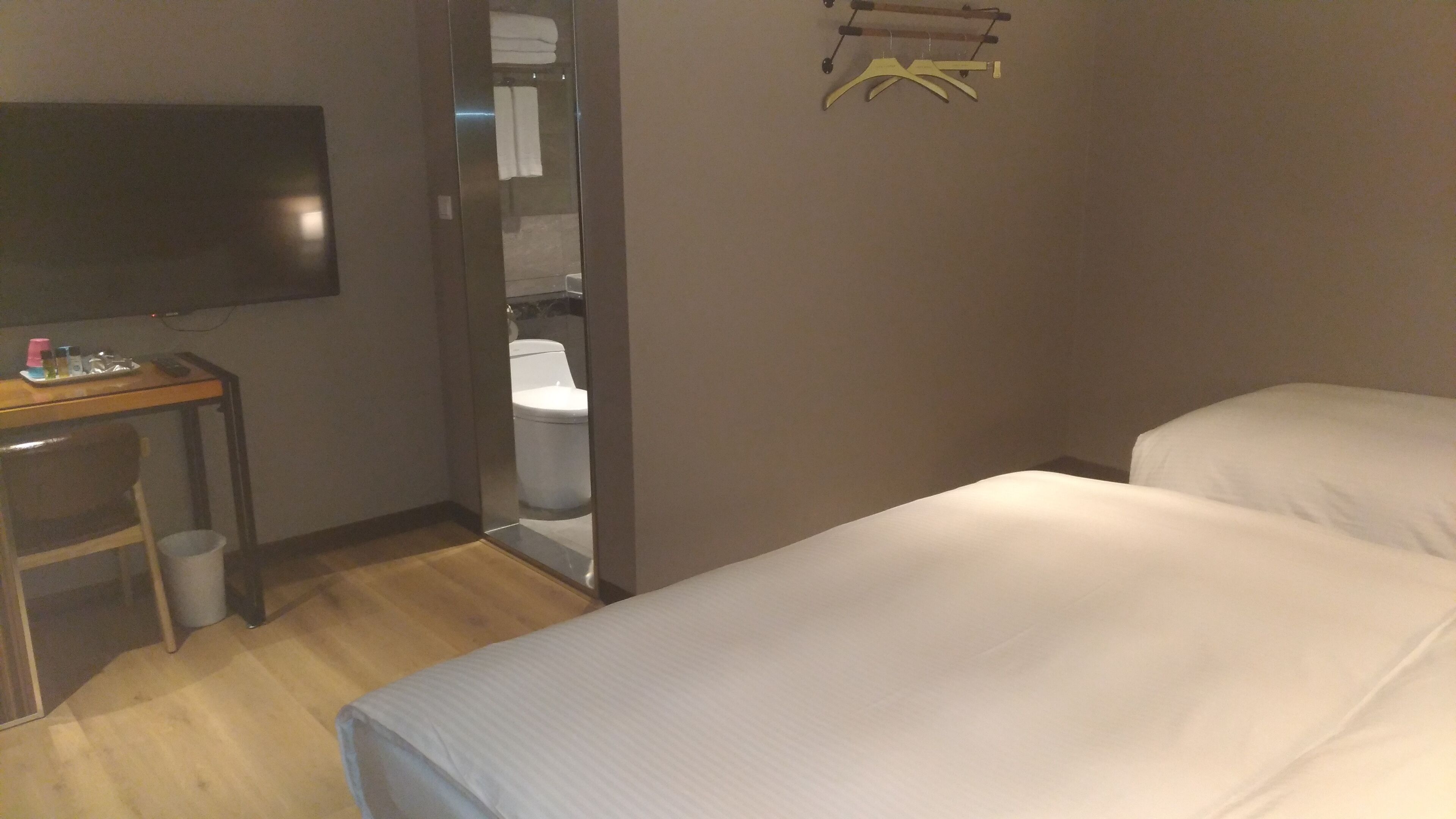 A hotel room with a bed, a desk with a TV, and a bathroom visible through an open door.