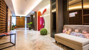 A modern lobby with a sofa featuring a Beatles-themed cushion, a wooden reception desk, and a colorful abstract wall. - Lucky Apple Hotel (Taipei)