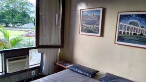 A hotel room with a bed, a small table, a radiator, and two framed pictures on the wall. - Apartamento Piccola Porto Bracuhy (Angra dos Reis)