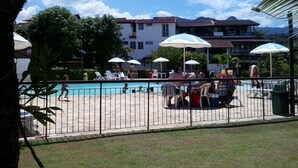 A pool area with lounge chairs and umbrellas, surrounded by a fence. - Apartamento Piccola Porto Bracuhy (Angra dos Reis)