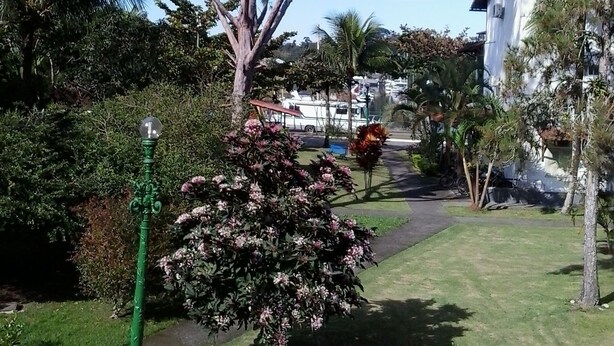 A pathway lined with trees and shrubs, a green street lamp, and a white building in the background. - Apartamento Piccola Porto Bracuhy (Angra dos Reis)