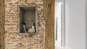 A brick wall with a small shelf containing books and candles.