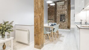 A modern kitchen with white cabinets, a brick wall, and a dining area with a white table and chairs.