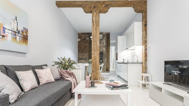 A modern living room with a grey sofa, white coffee table, and a TV on a white stand.