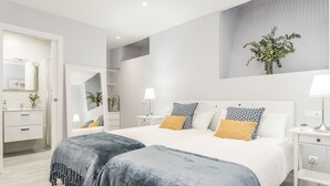 A modern bedroom with two beds, a large mirror, bedside tables, and a wall-mounted plant.