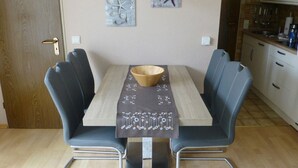 A dining area with a wooden table, two grey upholstered chairs, a wooden bowl, and a table runner with a pattern.