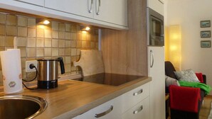 A compact kitchen with white cabinets, a stainless steel kettle, and a microwave.