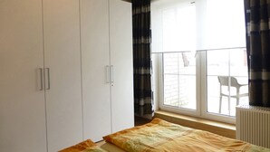 A bedroom with a large wardrobe, a window with curtains, and a view of the outside balcony.