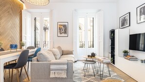 Una sala de estar moderna con un sofá, una mesa de comedor, sillas, un televisor y obras de arte en las paredes.