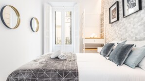 Un dormitorio con una cama, dos espejos en la pared, un aparador y una puerta que da a un balcón.