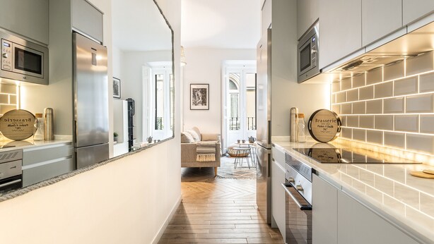 Una cocina moderna con electrodomésticos de acero inoxidable, piso de madera con patrón de espiga y un comedor con mesa y sillas redondas.