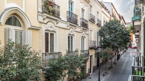 Una calle estrecha bordeada de edificios con balcones y barandillas de hierro forjado, además de macetas con flores.