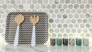 Un salpicadero de cocina con baldosas hexagonales y una tabla de cortar estampada con dos utensilios de madera.