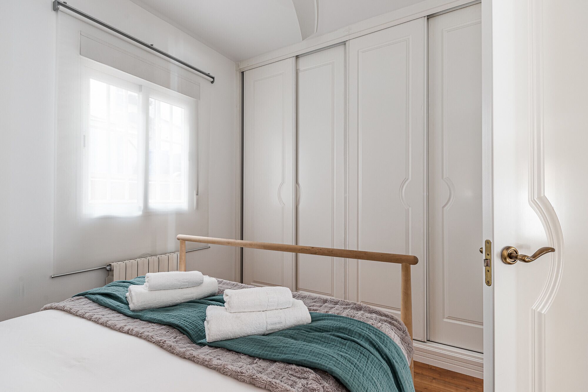 A bedroom with a bed, a window, a wardrobe, and a door.