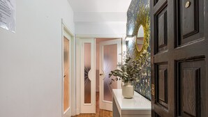 A hallway with a white door, a wooden floor, and a vase with dried plants on a white counter. - Waou La Latina II - Alquiler Corta Duración (Madrid)