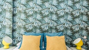 A bedroom with a bed, two yellow pillows, a blue headboard, and a tropical leaf wallpaper. - Waou Gran Via I - Alquiler Corta Duración (Madrid)