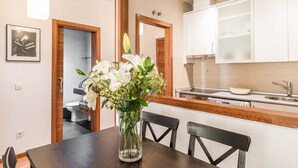 A modern kitchen with white cabinets, a wooden countertop, and a dining area with a dark wooden table and chairs. - Waou Gran Via I - Alquiler Corta Duración (Madrid)