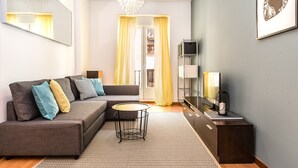 A modern living room with a grey sofa, a small round table, and a TV on a stand. - Waou Gran Via I - Alquiler Corta Duración (Madrid)